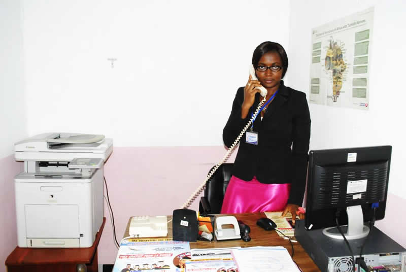 Secrétariat / Secrétaire / Assistante administrative répondant au téléphone débout derrière son bureau.